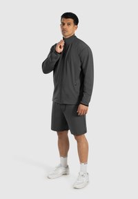 Donkergrijze sportjack met hoge kraag, rits aan de voorkant en bijpassende shorts, met een gladde textuur en een aansluitend ontwerp.