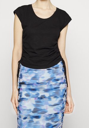 Kobieta ubrana w czarny marszczony top z krótkim rękawem oraz spódnicę z wysokim stanem w niebiesko-fioletowy abstrakcyjny wzór.
