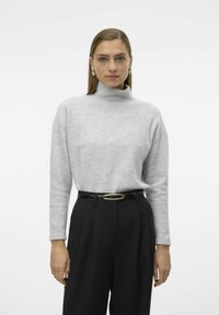 Pull à col montant gris clair en matériau doux, associé à un pantalon noir taille haute avec une fine ceinture rehaussée d'or. Design simple.