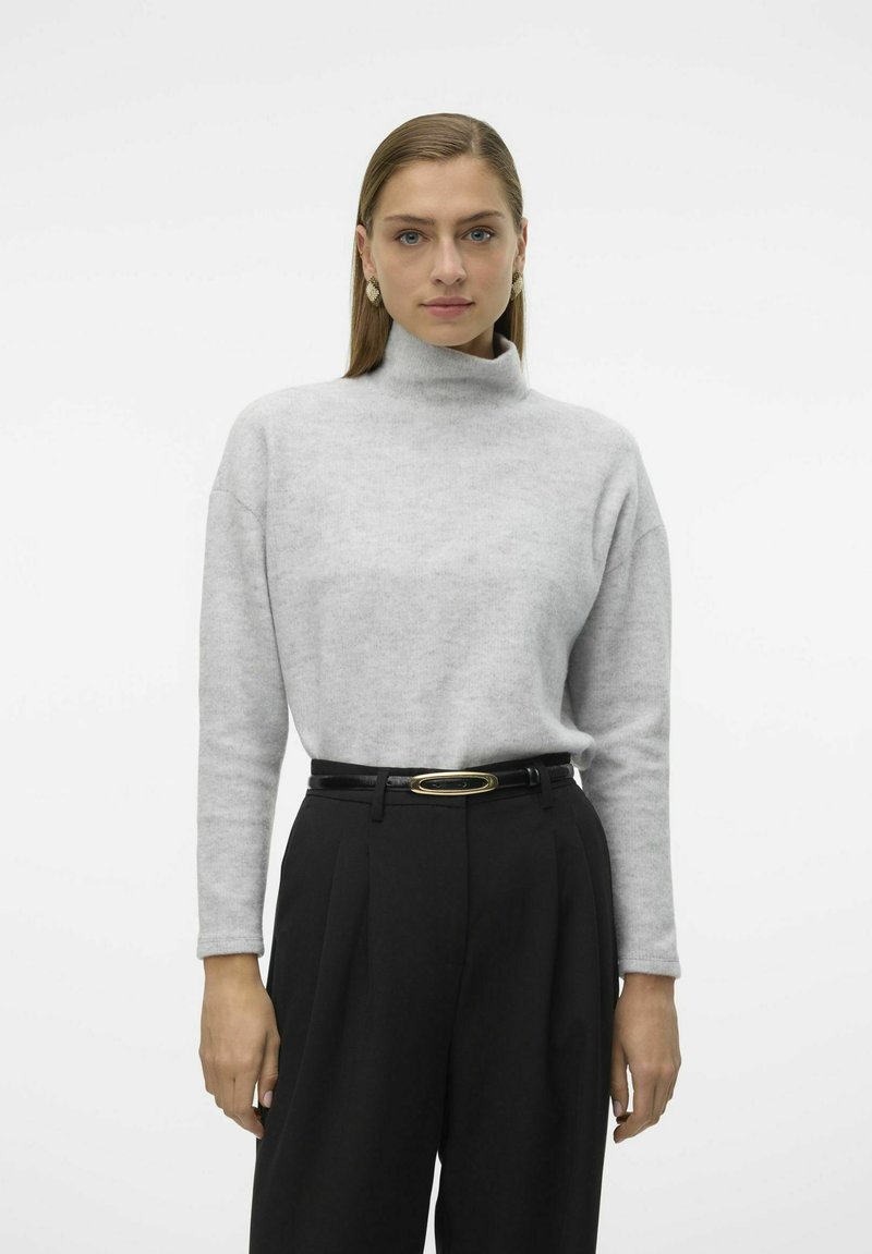Pull à col montant gris clair en matériau doux, associé à un pantalon noir taille haute avec une fine ceinture rehaussée d'or. Design simple.