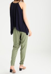 Mörkblå ärmlös topp med avslappnad passform, kombinerad med ljusgröna byxor. Modellen står i minimalistic footwear och visar upp outfitens färgkontrast.