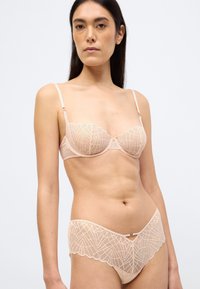 Γυναικείο αχνούδωτο σουτιέν με διαφάνειες, γεωμετρικά μοτίβα και ρυθμιζόμενους ιμάντες. Συνοδευτικό εσώρουχο από δαντέλα με κυματιστές άκρες και διακοσμητικό φιόγκο στο κέντρο.