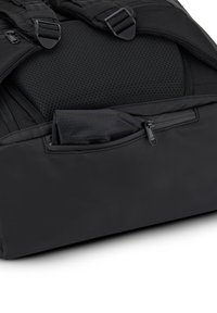 Fekete hátizsák párnázott hátsó panelekkel és állítható pántokkal, amelynek egyik oldalsó zsebe cipzárral részben nyitva van, és szövet lóg ki belőle.