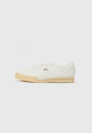 White leather sneakers with a textured surface, beige rubber sole, lace-up design, and subtle logo detail on the side.