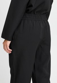 Svarta byxor med en slät yta, elastisk midja och sidofickor. Designen erbjuder en lös passform och enkla, rena linjer.