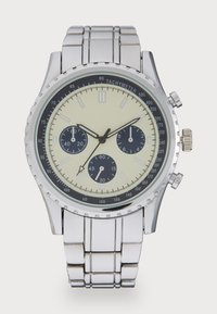 Montre chronographe en acier inoxydable argenté avec un boîtier rond, un cadran crème, des sous-cadrans noirs, une échelle tachymétrique et un bracelet à maillons poli.