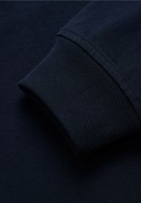 Camisa de algodón de manga larga azul marino, con detalles que muestran un puño acanalado y una textura suave; costura visible a lo largo del borde.