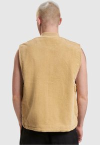 Gilet sans manches en velours côtelé beige clair. Doté d'un col montant et de poches sur les côtés ; texture lisse avec une coupe légèrement ample.