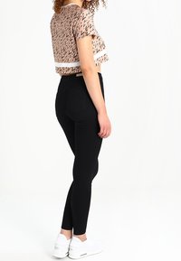 Top rosa recortado con un patrón geométrico y una franja blanca, combinado con leggings negros y zapatillas blancas. La modelo se encuentra de lado.