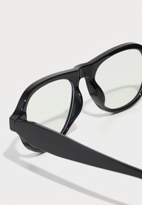 Ochelari de soare din plastic negru cu rame supradimensionate, lentile clare și tâmple groase, având un finisaj lucios și un design unghiular.