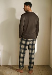 Brun langærmet top med en rund hals, parret med ternede pyjamasbukser i beige og marineblåt. Bukserne har en elastisk manchet ved anklen.