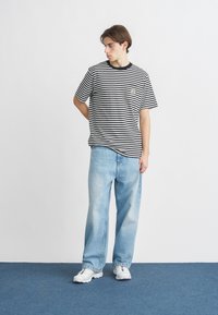 Μπλούζα με κοντά μανίκια και μαύρες και άσπρες ρίγες, με στρογγυλή λαιμόκοψη. Συνδυάζεται με ανοιχτό μπλε, φαρδιά τζιν και λευκά αθλητικά παπούτσια.