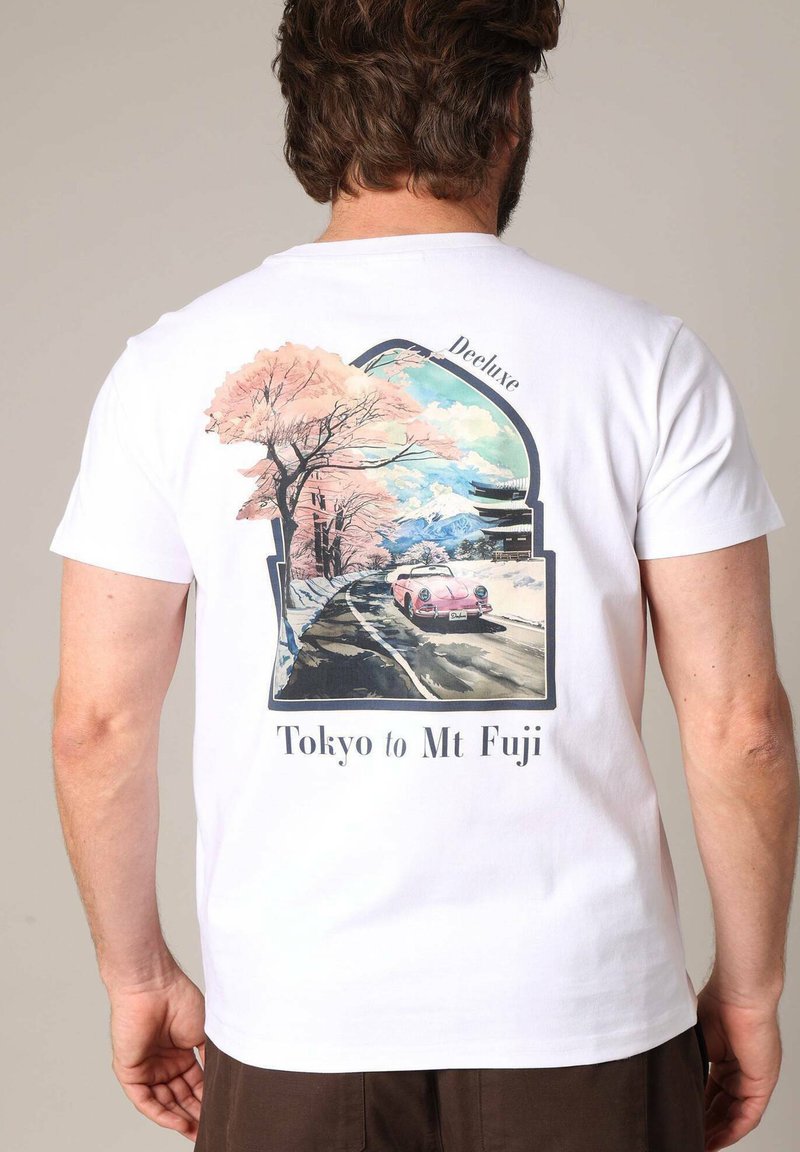 T-shirt en coton blanc avec un graphique coloré représentant des cerisiers en fleur et une voiture rose, accompagné du texte "De Tokyo au Mont Fuji" en dessous du design.