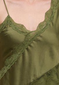 Gros plan d'une camisole en satin vert avec un galon en dentelle le long de l'encolure, des bretelles et de la couture diagonale.