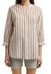 Chemise à rayures de couleur pêche clair et blanche, avec un col en V, des manches trois-quarts et des poignets froncés, fabriquée en tissu doux.