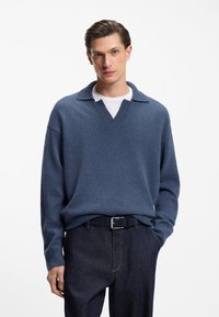 Blue knitted pullover sweater with a soft texture, featuring a wide collar and a V-neck design, paired with dark jeans.