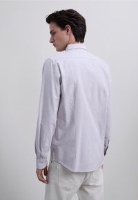 Langærmet skjorte i lyse lilla og hvide striber med krave, knapmanchetter og afrundet kant. Diskrete teksturelle detaljer.