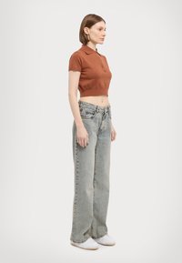 Brun kort polo med korte ermer, kombinert med løstsittende lyseblå jeans og hvite sneakers, som skaper et avslappet antrekk.