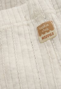 Crèmekleurige geribde tricotstof met een klein opgenaaid beige en bruin label waarop "Cookie Club Noppies" staat.