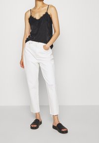 Černá saténová košilka s krajkovým lemem, spárovaná s bílými roztrhanými džíny rovného střihu a černými plochými sandály. Jednoduchý a decentní design.