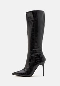 Svarta knähöga stövlar med ett glansigt krokodilmönster, spetsig tå, hög stilettkloss och slät textur. Sömdetalj synlig längs sidan.