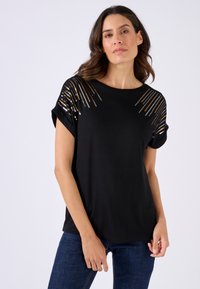 Zwarte t-shirt met korte mouwen heeft een ronde halslijn en paillettenaccenten die in lijnen op de schouders zijn gerangschikt, wat zorgt voor een textuurcontrast.