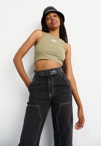 Top corto de tirantes verde oliva con un logo blanco; pantalones de pierna ancha de cintura alta negros con costuras blancas en contraste y grandes bolsillos.