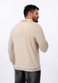 Sweatshirt beige à col, avec une texture lisse, des manches longues et une couture horizontale dans le dos.