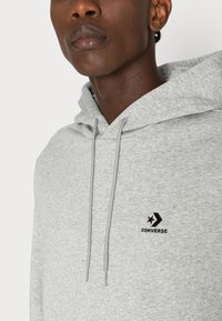Grijze katoenen hoodie met een voorkantzak, trekkoord en geborduurd zwart Converse-logo op de borst. Zachte textuur, casual pasvorm.