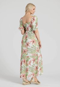 Maxiklänning med puffärmar, blommigt mönster i rosa och gröna löv på vit tyg, smockad byst och flerlagers volangkant; gyllene espadrillos.