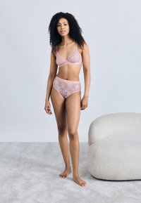 Σετ ροζ ανοιχτόχρωμης δαντέλας εσωρούχων που περιλαμβάνει ένα μπραλετάκι με τριγωνικά μπούστα και ασορτί ψηλόμεσο σλιπ, και τα δύο με λουλουδένιο σχέδιο και απαλό περίγραμμα.