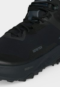 Κοντινό πλάνο μαύρου αθλητικού παπουτσιού Gore-Tex με μαύρα κορδόνια, υφασμένη επάνω επιφάνεια και χοντρή σόλα με ετικέτα EGO Max και Vibram.
