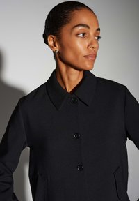 Zwarte wollen jas met een kraag, knopen aan de voorkant en zijzakken. Gladde textuur en nauwsluitende pasvorm, voor een gestructureerde uitstraling.