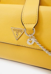 Borsa a mano in pelle gialla con logo Guess triangolare, ferrature argentate e dettaglio con catena intrecciata. Finitura strutturata con bordo a contrasto.