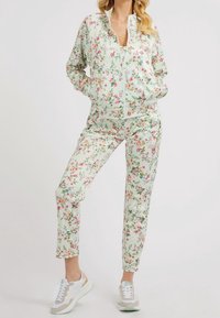 Trainingspak met bloemenprint in lichtgroen met een jas met ritssluiting en nauwsluitende broek. Voorzien van delicate roze en blauwe bloemen. Gecombineerd met witte sneakers.