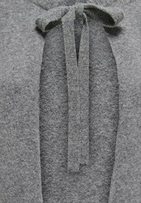 Pull gris avec un tricot texturé, présentant un col en V profond et une fermeture à nouer à l'avant en tissu gris assorti.