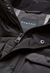 Black puffer jacket with a smooth finish, featuring a zipper closure, logo patch, and contrasting red accents in the stitching and hardware.