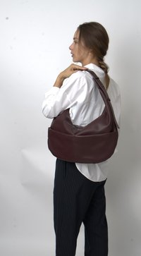 Burgundy leather handbag with a slouchy silhouette, adjustable strap, and smooth texture, worn over the shoulder. Stripes on pants.