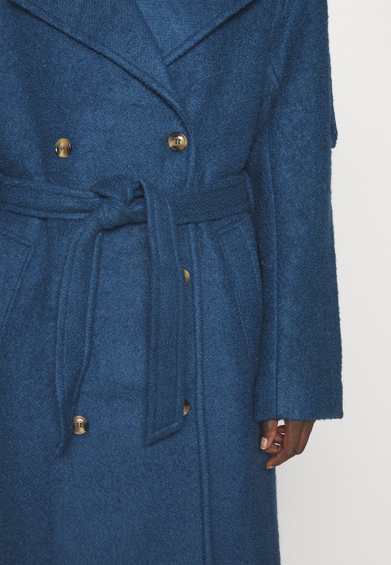 Niebieski płaszcz o teksturowanej powierzchni z paskiem w talii, dużymi klapami i złotymi guzikami, prezentujący podwójnie zapięty krój oraz szerokie rękawy.