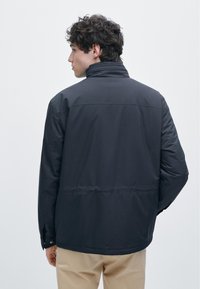 Donkergekleurde, gewatteerde jas met een hoge kraag, lange mouwen en verstelbare manchetten. Gladde textuur zonder zichtbare patronen of hardware-details.