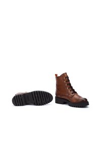 Bottines en cuir marron, à bout rond, avec lacets, œillets dorés et une semelle en caoutchouc noir robuste. Elles possèdent une boucle à l'arrière pour un enfilage facile.