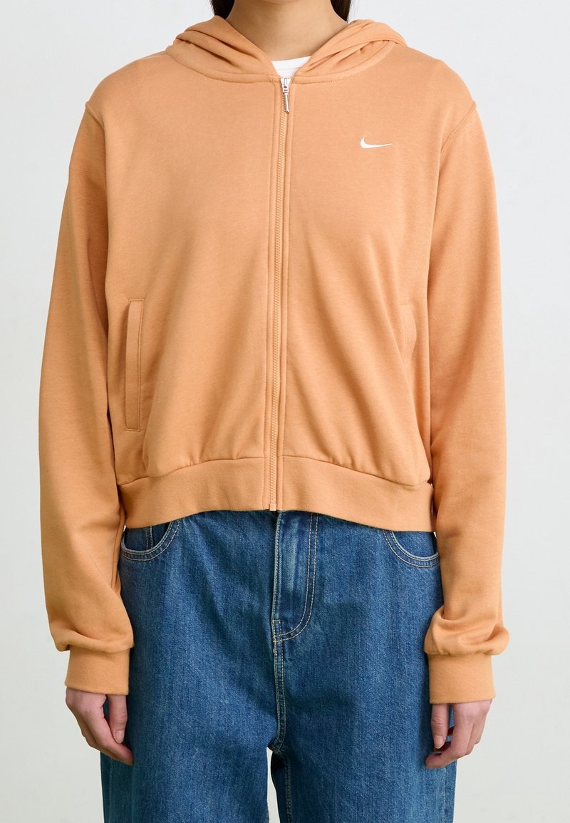 Orange zip-up hoodie i mjukt tyg, med en känguruficka, ribbad nederdel och en liten vit logotyp på bröstet.