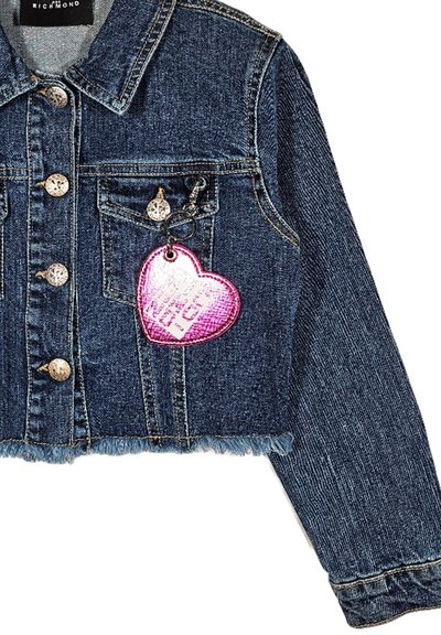 Giacca di jeans cropped di colore blu scuro con bottoni argentati, caratterizzata da un'etichetta a forma di cuore rosa con testo e dettagli a frange all'orlo.