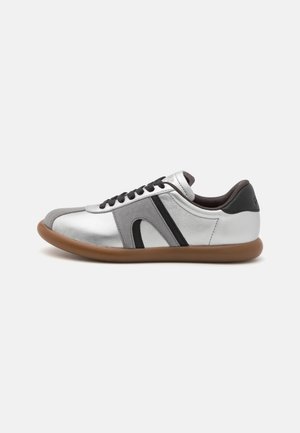 Sneaker en cuir argenté avec des accents gris et noirs, bout rond, lacets noirs et semelle en caoutchouc marron. Présente des surfaces lisses et texturées.