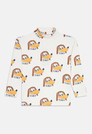 Haut à manches longues blanc arborant un motif répétitif de visages de chiens de dessin animé et le mot "TINY" en bleu, avec un col montant.