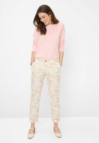 Sweatshirt rose clair à col rond, pantalon crème à motifs avec un design floral rose et doré, et chaussures plates beiges avec un détail de bride.