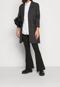 Svart och grå rutad kavaj med axelvaddar, enkel knappstängning, tillsammans med en vit skjorta, svarta byxor och kraftiga svarta skor.