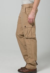 Beige cargobroek met meerdere zijzakken, knoopsluitingen, rechte pijpen en lichtgewicht stof. Gecombineerd met bruine wandelschoenen.