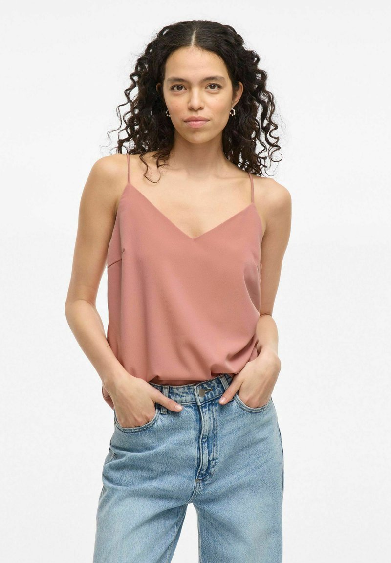 Camisola din satin de culoare roz, cu bretele subțiri și decolteu în V. Asortată cu blugi din denim de culoare albastră deschisă, cu talie înaltă, evidențiind o croială lejeră.