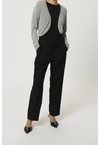 Cardigan gris clair coupé porté sur un haut noir, associé à un pantalon noir taille haute. Mules noires à bout pointu ornées de détails métalliques décoratifs.